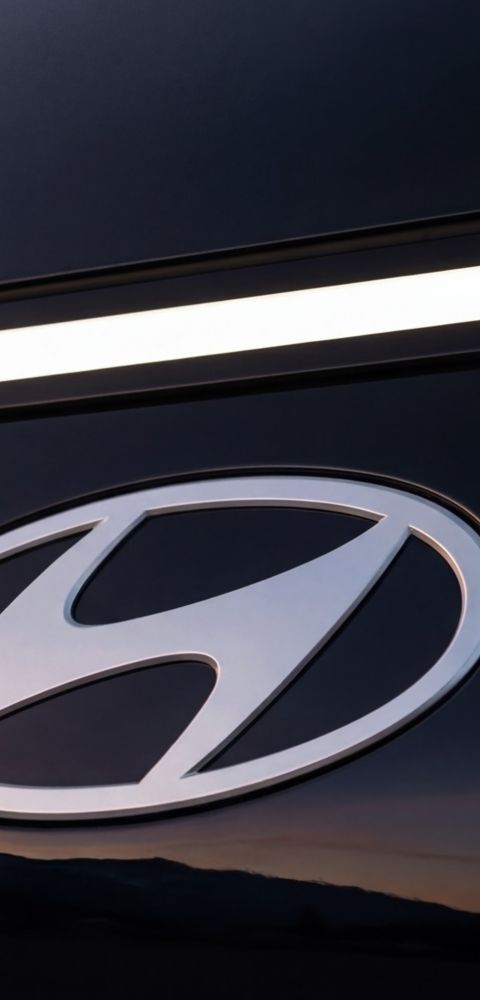Hyundai STARIA Electric front emblem detail with LED light strip at sunset.