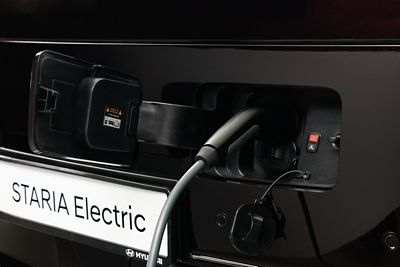 STARIA Electric töltőaljzata, csatlakoztatott töltőkábellel, közeli felvételen.