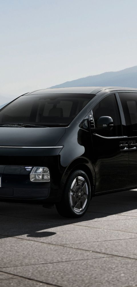 Hyundai STARIA Electric parked outdoors with mountain landscape in the background, viewed from the front three-quarter angle.