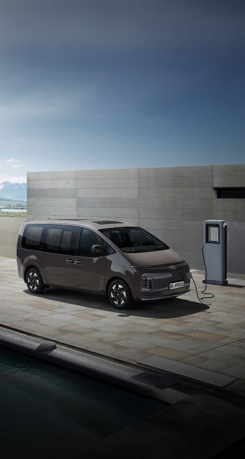 Hyundai STARIA Electric, der draussen mit einer EV-Ladestation verbunden ist, hebt den bequemen Zugang zum Laden hervor.