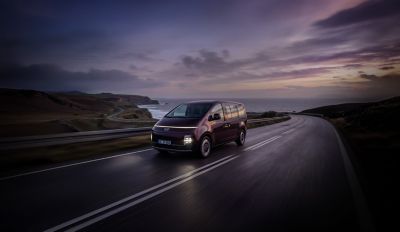 Der Hyundai STARIA Elektro fährt bei Sonnenuntergang entlang einer Küstenstraße. 