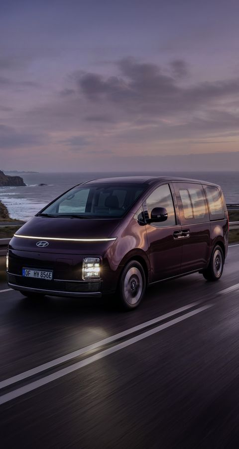 Hyundai STARIA Electric auf einer Küstenstrasse bei Sonnenuntergang.