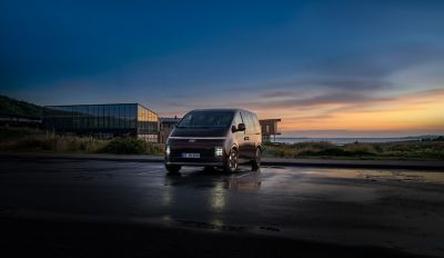 Hyundai STARIA Electric minibuss sedd framifrån, parkerad framför en modern byggnad i skymningsljus med texten ”Style, space and flexibility” över bilden.