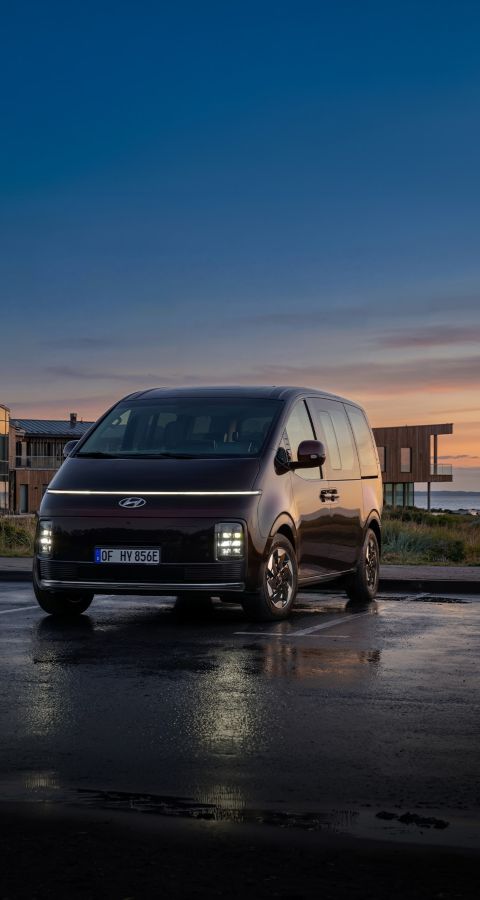 Hyundai STARIA Electric minibuss sedd framifrån, parkerad framför en modern byggnad i skymningsljus med texten ”Style, space and flexibility” över bilden.