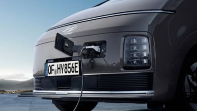 Close-up of the Hyundai STARIA Electric front end with open charging port and plugged-in charging cable.
