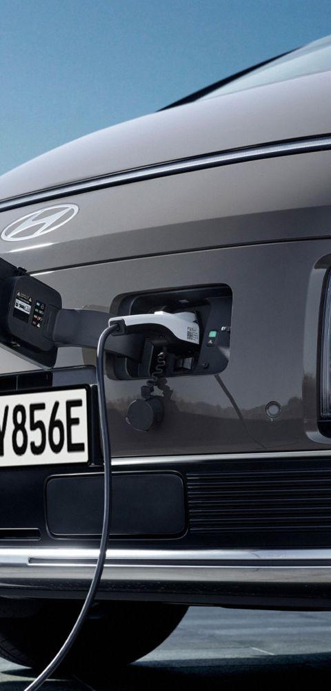 Close-up of the Hyundai STARIA Electric front end with open charging port and plugged-in charging cable.