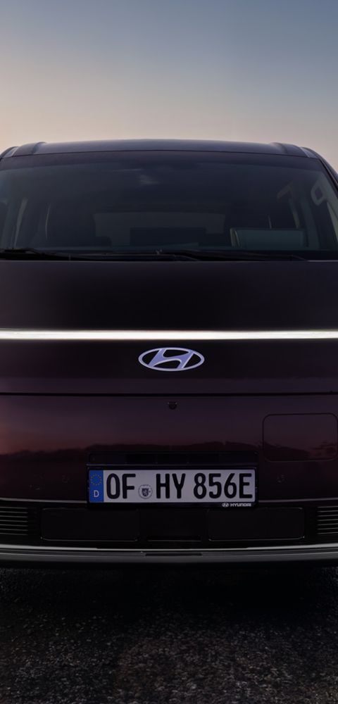 Front view of the Hyundai STARIA Electric with illuminated LED lights at sunset.