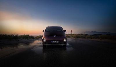 Front view of the Hyundai STARIA Electric with illuminated LED lights at sunset.