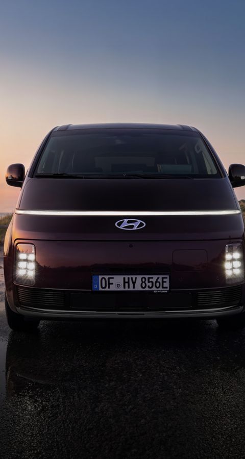 Front view of the Hyundai STARIA Electric with illuminated LED lights at sunset.