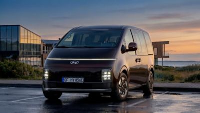 Hyundai STARIA Electric, van voren gezien, met een zonsondergang op de achtergrond.