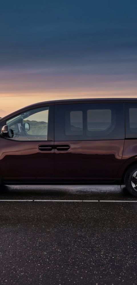 Side profile of the Hyundai STARIA Electric parked by the ocean at dusk.