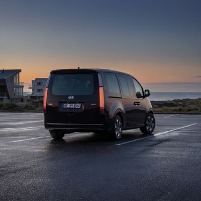 Hyundai STARIA Electric modern tengerparti házak mellett parkol. Hátulnézetből.