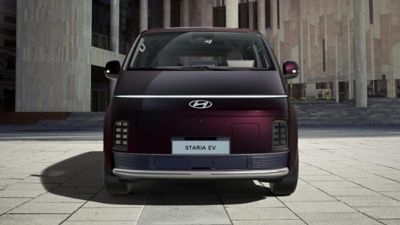Front view of Hyundai STARIA Electric passenger van outside a modern building, highlighting an all-electric fleet solution for passenger transport.