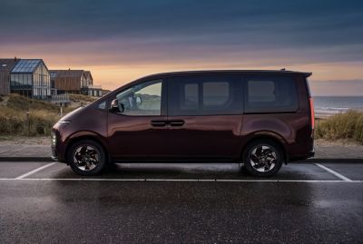 Side profile of the Hyundai STARIA Electric parked by the ocean at dusk.