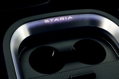 Illuminated Hyundai STARIA Electric branding near built-in cup holders in the center console.