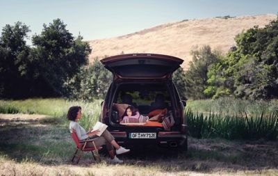 Žena čítajúca rozprávku dieťaťu vo vnútri modelu Hyundai Santa Fe s veľkým otvorom dverí batožinového priestoru.