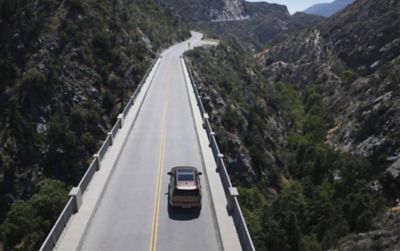 The Hyundai SANTA FE from above, driving on a road the mountains.