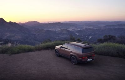 Scène de coucher de soleil avec Hyundai SANTA FE Nouvelle Génération garé sur une crête de montagne.