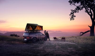 Twee mensen leunend tegen Hyundai SANTA FE met daktent, kijkend naar zonsondergang.