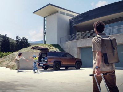 A woman hugs a kid in front of the Hyundai Santa Fe and its large open tailgate. 