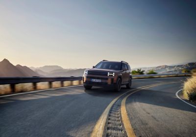 The Hyundai Santa Fe driving a curvy road with mountains in the background. 