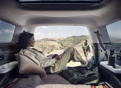  A woman leaning back, relaxing and reading a book inside the tailgate of the  Hyundai Santa Fe.