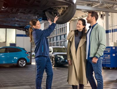 Hyundai servicing mechanic talking to two car owners in the workshop.