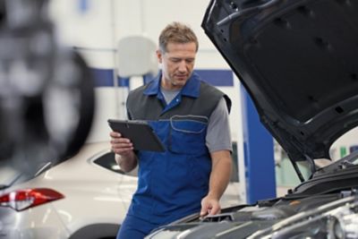  Independent operator inspecting a vehicle engine using a tablet in a workshop.