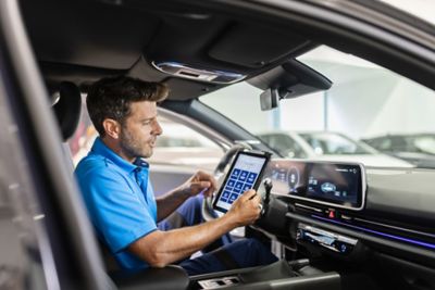 Hyundai Service technician using a tablet inside a Hyundai vehicle to perform diagnostics.