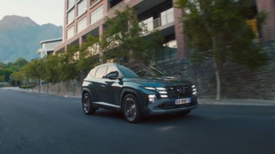 Hyundai TUCSON vista lateralmente mentre percorre una strada alberata