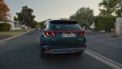 The Hyundai TUCSON Plug-in Hybrid is seen from the side back driving down the road.