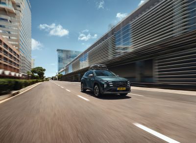 Hyundai TUCSON met dakkoffer rijdend langs modern gebouw.