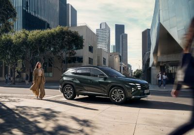 Hyundai TUCSON zaparkovaný ve městě a kolem něj procházející žena.