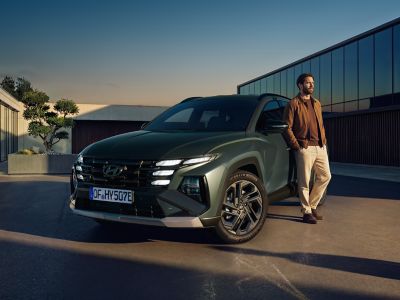 A man leaning on the Hyundai TUCSON Plug-in Hybrid parked in front of the building.