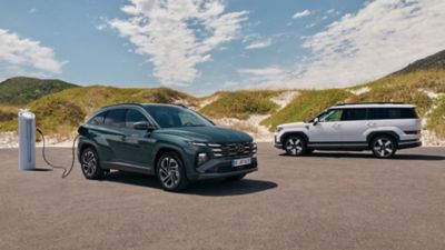 Hyundai TUCSON Plug-in Hybrid and SANTA FE Plug-in Hybrid parked near an EV charging station.