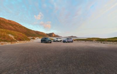 TUCSON, SANTA FE and KONA EV parked, hillside view background.