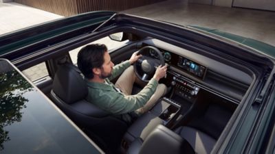 Pohled před otevřenou panoramatickou střechu na muže sedící za volantem modelu TUCSON.