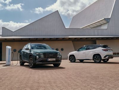 Hyundai TUCSON Plug-in Hybrid and Hyundai TUCSON Hybrid SUVs parked beside an EV charging station.