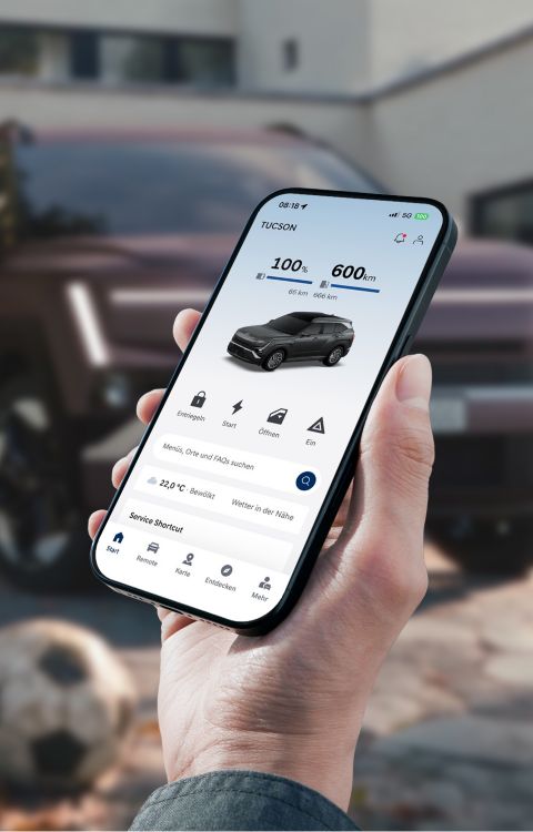 Une vue rapprochée d'une main tenant un téléphone mobile avec en arrière-plan le Hyundai TUCSON.