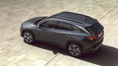 Nuevo Hyundai TUCSON Híbrido Enchufable cargándose en la entrada de una casa.