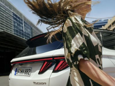 Eine Frau in grün-weißem Kleid geht mit wehenden Haaren hinter dem Hyundai TUCSON vorbei.