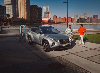 Hyundai TUCSON Plug-in-Hybrid vicino una stazione di ricarica con accanto ragazzi che corrono
