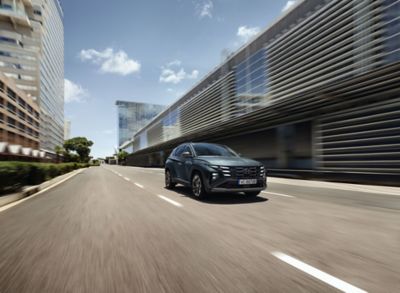 Hyundai TUCSON Hybrid jadący ulicą w mieście na tle nowoczesnych budynków.
