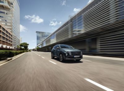 The Hyundai TUCSON Plug-in Hybrid driving down a city street with modern buildings visible.