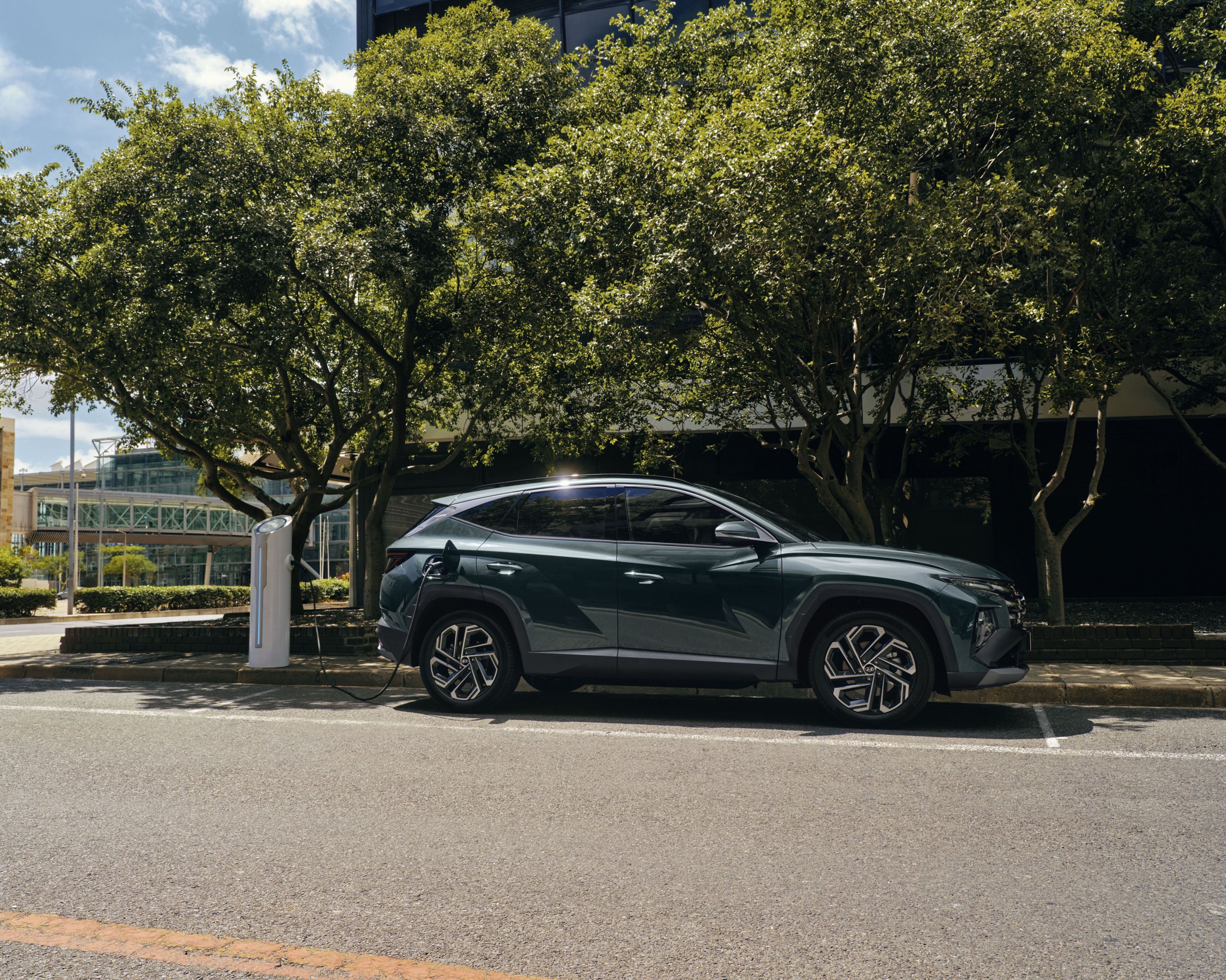 The Hyundai TUCSON Plug-in Hybrid plugged in to charge parked under some trees. 