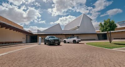 Two Hyundai TUCSON Plug-in Hybrid SUVs parked in front of a big, elegant house. 