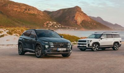 Twee Hyundai SUVs geparkeerd naast een baai bij een berg , Tucson, en Santa Fe.