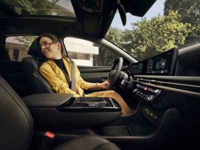 	Žena sedící na sedadle řidiče vozu Hyundai TUCSON Hybrid a ohlížející se přes rameno.