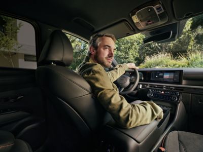 A man sitting in the driving seat of the Hyundai TUCSON Hybrid, looking back over his shoulder.