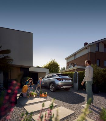 Imagen del TUCSON Híbrido enchufable a la entrada de una casa moderna con una familia alrededor.